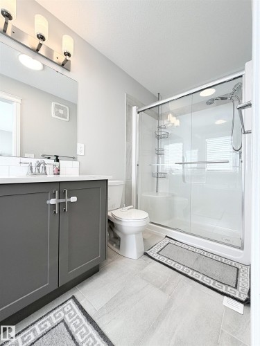 Bathroom featuring a glass-enclosed shower, a white vanity with a gray base, a wall-mounted light fixture, and light-toned tile flooring - 1003 Goldfinch Way Nw, Edmonton, AB 