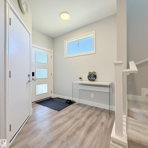 Entryway featuring wood-finish flooring, a contemporary front door with three frosted glass panels, a rectangular window, and a carpeted staircase with white railings - 1003 Goldfinch Way Nw, Edmonton, AB 