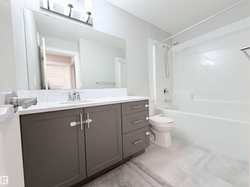 Contemporary bathroom featuring a dark gray vanity with a light countertop, subway tile backsplash, and a white tub with shower - 1003 Goldfinch Way Nw, Edmonton, AB 