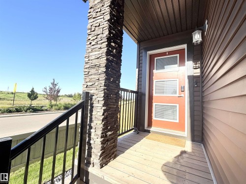 Covered front porch with wood-finish decking, stone-clad pillar, and black metal railing - 1003 Goldfinch Way Nw, Edmonton, AB 