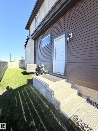 Brown horizontal siding exterior with a white entry door featuring horizontal paneling, concrete steps, and a compact grass area - 1003 Goldfinch Way Nw, Edmonton, AB 