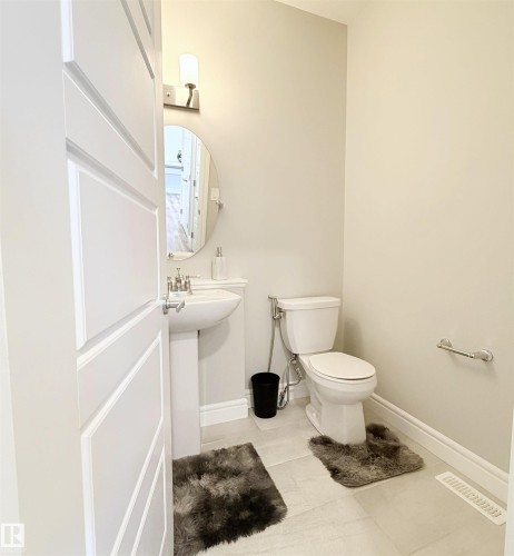 Pedestal sink with chrome faucet, wall-mounted light fixture, oval mirror, and tile flooring - 1003 Goldfinch Way Nw, Edmonton, AB 