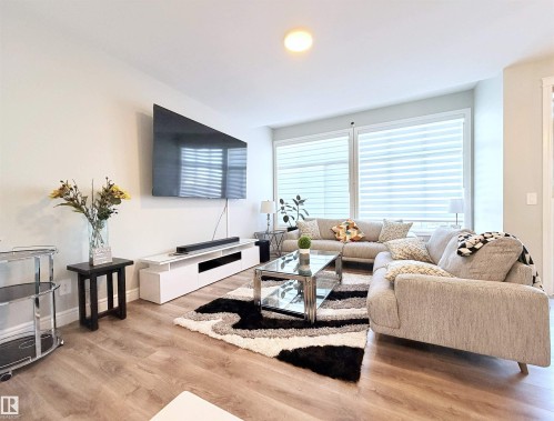 Wood-finish flooring, recessed ceiling lighting, large windows with horizontal blinds, and a wall-mounted flat-screen television - 1003 Goldfinch Way Nw, Edmonton, AB 