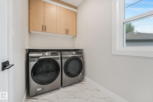 Dedicated laundry room featuring stainless steel front-load washer and dryer, natural light from large window, wood-finish cabinetry with brushed metal hardware, and tile flooring - 16 Middleton Close, Leduc, AB 