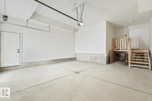 Spacious garage featuring a concrete floor, dedicated entry door, and elevated storage area - 16 Middleton Close, Leduc, AB 
