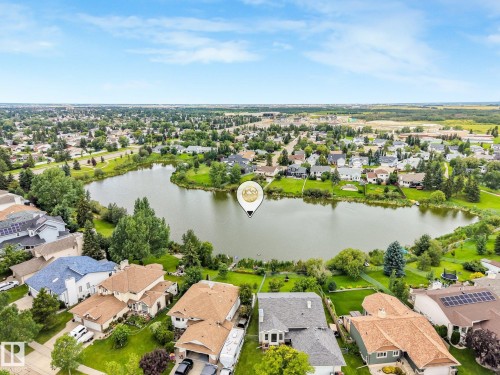 Aerial perspective showcasing a residential area with a prominent body of water, surrounded by green spaces and residential properties - 16 Middleton Close, Leduc, AB 