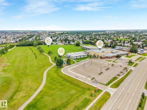 Expansive green space featuring a paved walking path, mature trees, and a community building - 16 Middleton Close, Leduc, AB 