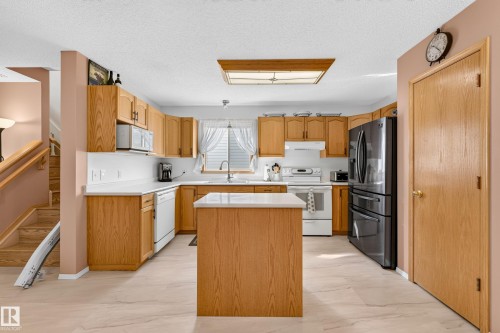Kitchen featuring wood-finish cabinetry, white countertops, a central island, and a stainless steel refrigerator - 1223 Gillespie Crescent Nw, Edmonton, AB 