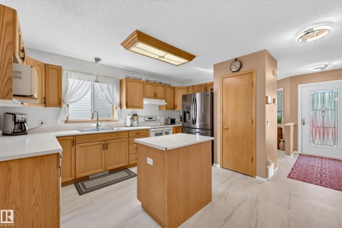 Kitchen featuring wood-finish cabinetry, stainless steel refrigerator, white countertops, center island, and wood-finish flooring - 1223 Gillespie Crescent Nw, Edmonton, AB 