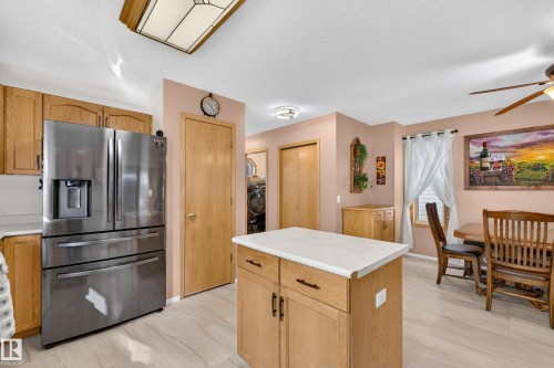 Stainless steel refrigerator with a built-in ice and water dispenser, wood-finish cabinetry, and a central island with white countertop - 1223 Gillespie Crescent Nw, Edmonton, AB 