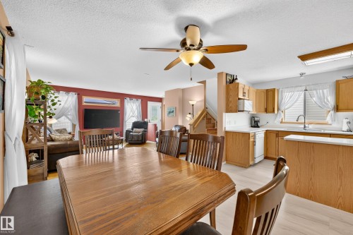 Open-concept living area with a ceiling fan, wood-finish flooring, and a kitchen featuring wood cabinetry, white countertops, and a stainless steel sink - 1223 Gillespie Crescent Nw, Edmonton, AB 