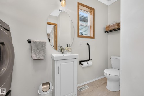 White vanity with integrated sink, oval mirror, and a wood-trimmed window - 1223 Gillespie Crescent Nw, Edmonton, AB 