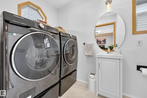 Integrated laundry machines, hexagonal window with wood-finish trim, round vanity mirror, single-door vanity with integrated sink, and wall-mounted lighting fixture - 1223 Gillespie Crescent Nw, Edmonton, AB 