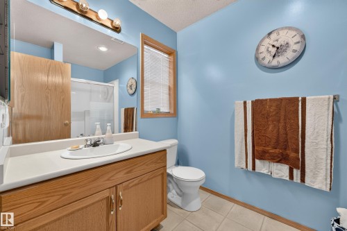 Wood-finish vanity with an integrated sink, broad mirror, and overhead vanity lighting - 1223 Gillespie Crescent Nw, Edmonton, AB 