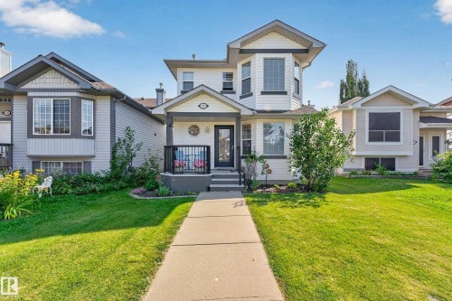 Exterior featuring light-toned siding, a front porch with black railings, a bay window, and a concrete walkway - 1223 Gillespie Crescent Nw, Edmonton, AB 