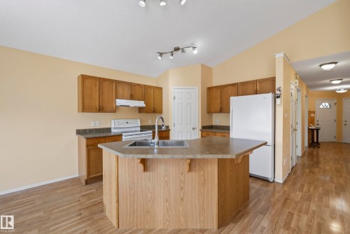 Kitchen featuring wood-finish flooring, wood cabinetry, a center island with sink, and white appliances - 15213 49A Street Nw, Edmonton, AB 