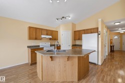 Kitchen featuring wood-finish flooring, wood cabinetry, a center island with sink, and white appliances - 