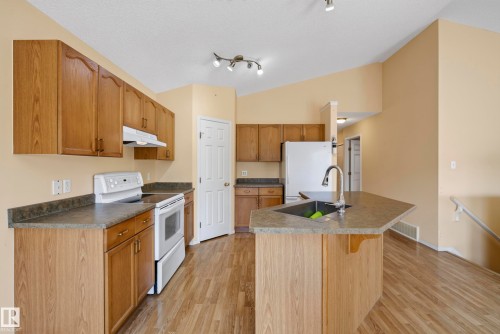 Kitchen featuring wood-finish cabinetry, solid surface countertops, a white appliance package, and a kitchen island with an undermount sink - 15213 49A Street Nw, Edmonton, AB 