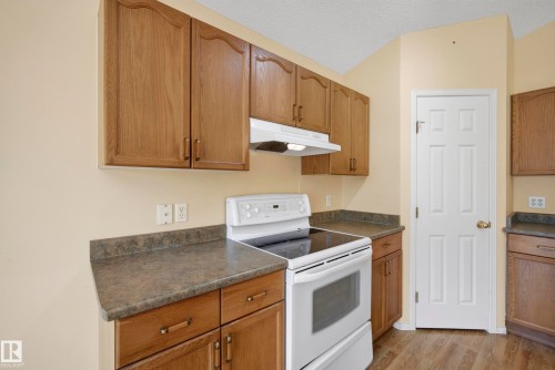 Wood-finish cabinetry, white range, dark countertops, white door, and wood-finish flooring - 15213 49A Street Nw, Edmonton, AB 