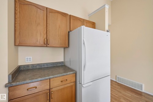 Wood-finish cabinetry with brass hardware, speckled countertop, and a built-in white refrigerator - 15213 49A Street Nw, Edmonton, AB 