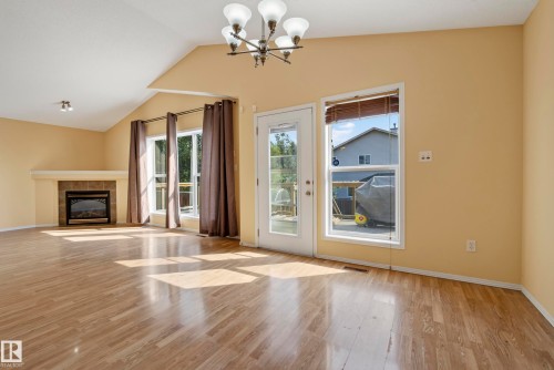 Vaulted ceiling, wood-finish flooring, built-in fireplace with stone-tile surround, multiple windows, and a glass-paneled exterior door - 15213 49A Street Nw, Edmonton, AB 