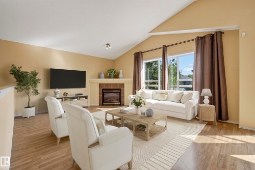 Vaulted ceiling in a spacious living area featuring wood-finish flooring, a tile-surround fireplace with mantel, and large windows - 15213 49A Street Nw, Edmonton, AB 