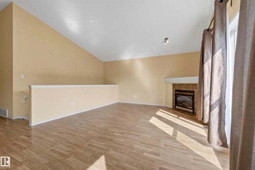 Vaulted ceiling, wood-finish flooring, tiled fireplace with mantel, and track lighting - 15213 49A Street Nw, Edmonton, AB 