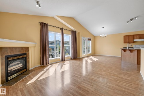 Vaulted ceilings, wood-finish flooring, fireplace with tile surround, large windows, and a built-in kitchen island - 15213 49A Street Nw, Edmonton, AB 