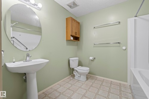 Pedestal sink with chrome faucet, oval mirror, wall-mounted light fixture, wood-finish wall cabinet, and patterned tile-look flooring - 15213 49A Street Nw, Edmonton, AB 