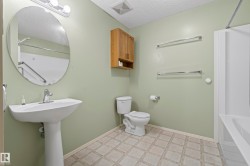 Pedestal sink with chrome faucet, oval mirror, wall-mounted light fixture, wood-finish wall cabinet, and patterned tile-look flooring - 