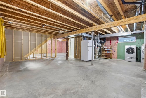 Unfinished basement featuring exposed wood joists, concrete flooring, framed wall sections, and a dedicated laundry area with appliances - 15213 49A Street Nw, Edmonton, AB 
