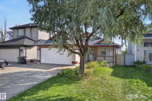 Front exterior featuring an attached garage, covered porch, and mature trees - 15213 49A Street Nw, Edmonton, AB 