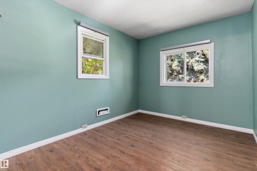 Serene bedroom showcasing soft turquoise walls, natural light from two windows with white trim, and warm wood-finish flooring - 5501 48 Avenue, Wetaskiwin, AB 