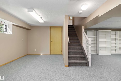 Carpeted lower level with a window, built-in shelving, and a stairway with a wood banister - 5501 48 Avenue, Wetaskiwin, AB 