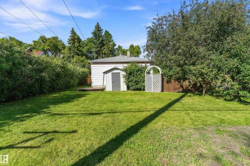 Expansive lawn with mature perimeter trees, a white detached shed, and a decorative white lattice gate - 5501 48 Avenue, Wetaskiwin, AB 