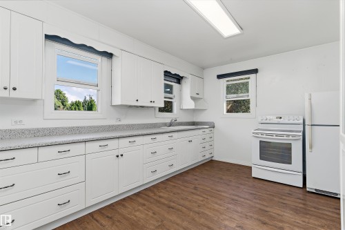 Kitchen featuring white cabinetry, speckled countertops, stainless steel sink, wood-finish flooring, and white appliances - 5501 48 Avenue, Wetaskiwin, AB 