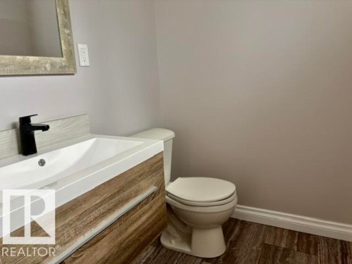 Floating vanity with wood-finish cabinetry, integrated rectangular sink, matte black faucet, and wood-finish flooring - 5133 45A Avenue, Vegreville, AB 
