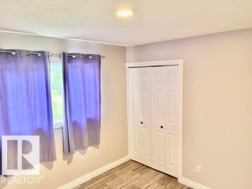 Recessed ceiling light, white bi-fold closet doors, wood-finish flooring, white trim, and a window with a white frame - 5133 45A Avenue, Vegreville, AB 