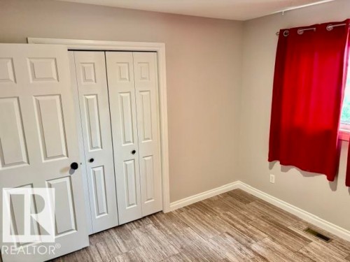 Wood-finish flooring with white trim, light gray painted walls, and white paneled bi-fold closet doors - 5133 45A Avenue, Vegreville, AB 