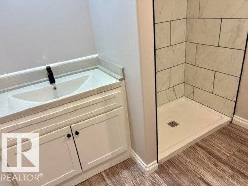 White vanity with integrated rectangular sink and matte black faucet, wood-finish flooring, and a tiled shower stall with a white base - 5133 45A Avenue, Vegreville, AB 