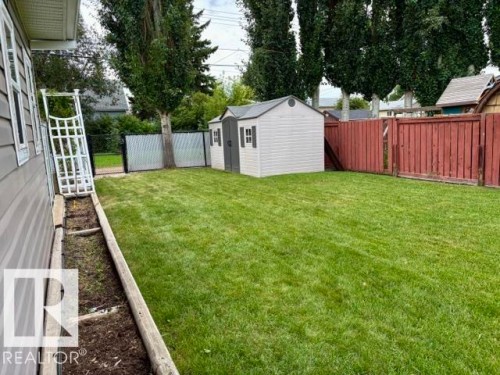 Expansive lawn space with a utility shed, bordered by a privacy fence and a dedicated planting bed - 5133 45A Avenue, Vegreville, AB 