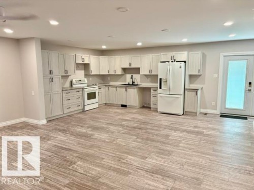 Spacious kitchen featuring extensive light cabinetry, contrasting hardware, a modern white appliance suite, and wood-finish flooring - 5133 45A Avenue, Vegreville, AB 