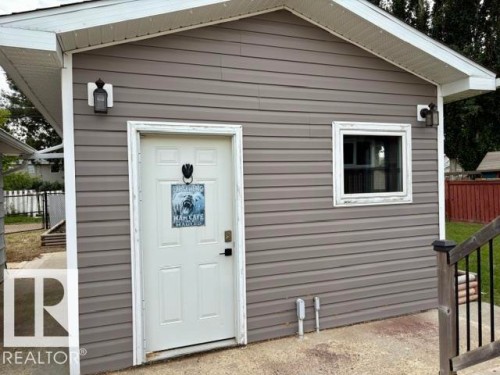 Gray horizontal siding exterior with a white entry door, window, and two exterior light fixtures - 5133 45A Avenue, Vegreville, AB 