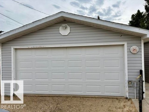 Single-panel garage door with horizontal siding exterior, gable roofline, and soffit lighting - 5133 45A Avenue, Vegreville, AB 