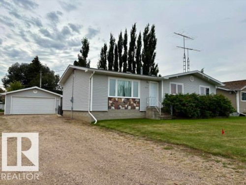 Light-toned siding exterior with stone-finish accent, attached garage, and gravel driveway - 5133 45A Avenue, Vegreville, AB 
