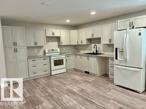 Kitchen featuring wood-finish flooring, light-toned cabinetry with dark hardware, a white electric range, a black sink with a matte black faucet, and a white French door refrigerator - 5133 45A Avenue, Vegreville, AB 