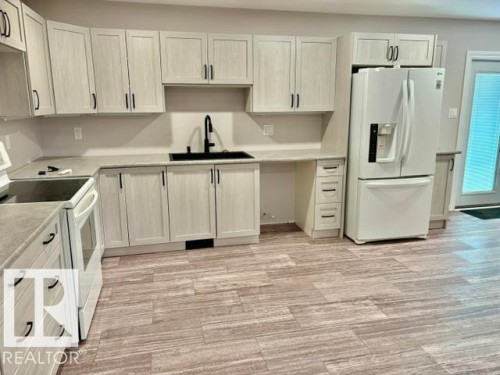 Kitchen featuring light wood-finish cabinetry, light grey countertops, a white refrigerator, a black sink, and wood-look flooring - 5133 45A Avenue, Vegreville, AB 