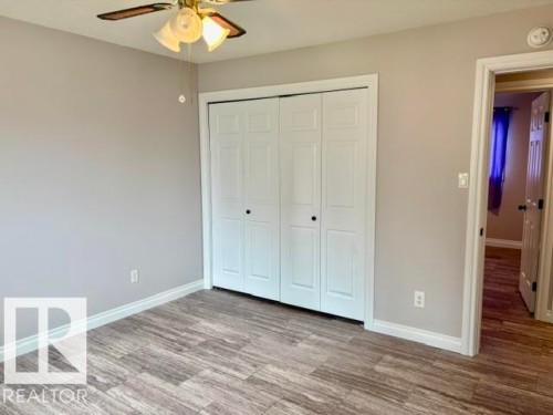 Wood-finish flooring, white bi-fold closet doors, ceiling fan with light fixture, and neutral wall paint - 5133 45A Avenue, Vegreville, AB 