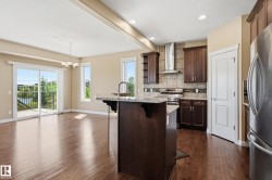Open-concept kitchen and living area featuring wood-finish flooring, a kitchen island with stone countertop and integrated sink, stainless steel appliances, and dark wood cabinetry - 