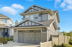 Multi-level home featuring grey siding, stone accents, and a two-car garage with transom windows - 